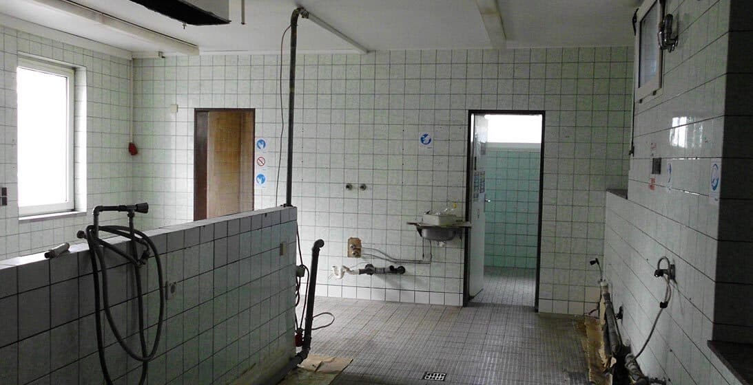 Alter gefliester Raum mit freiliegenden Leitungen vor der Sanierung